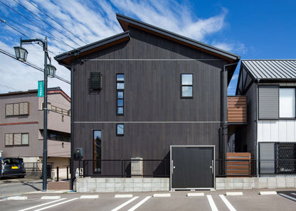 Modern black wooden house exterior with large windows against a blue sky, showcasing contemporary architectural design.